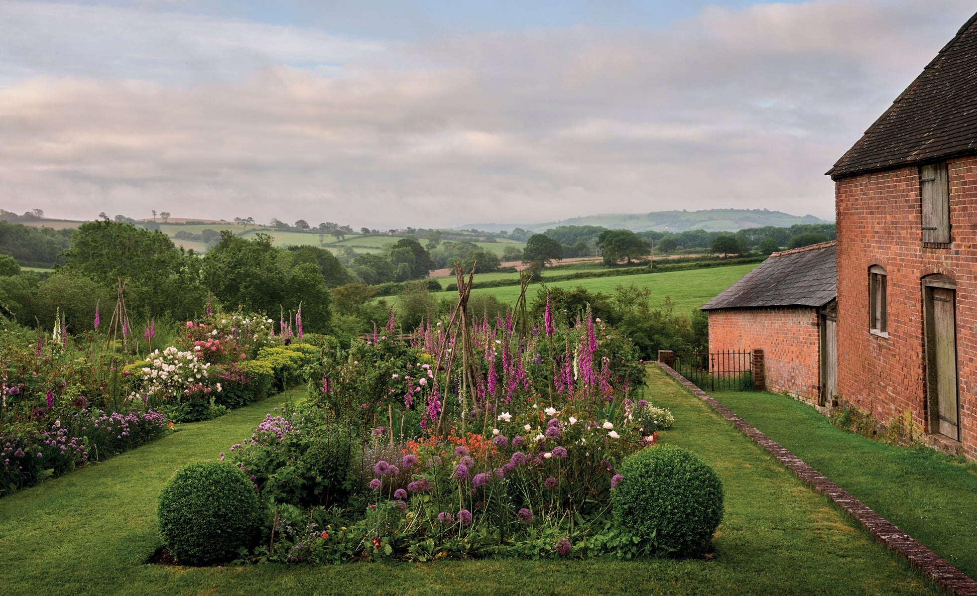 Bettiscombe Manor Dorset – Staudenbeet mit Fingerhut und Allium vor walisischer Hügellandschaft, Pastorale Gärten